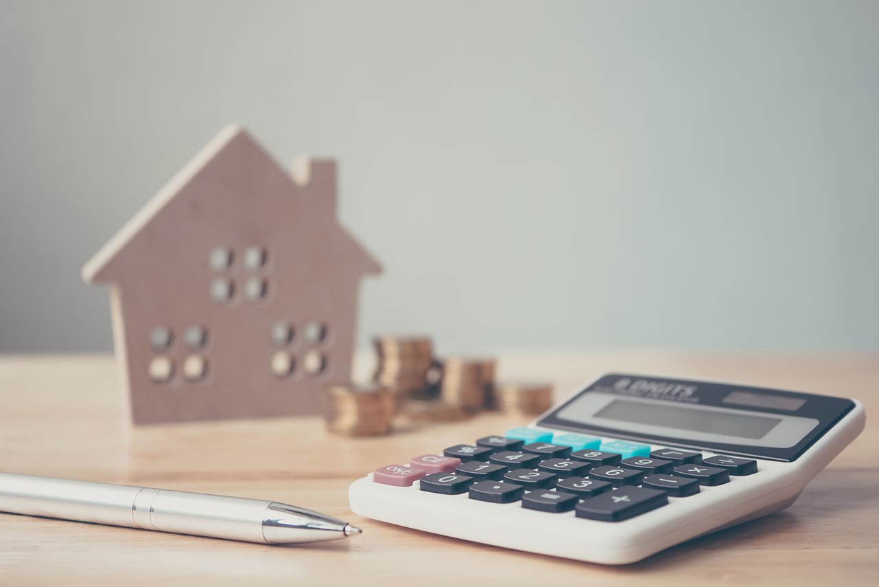 Calculator with wooden house and coins stack and pen on wood table